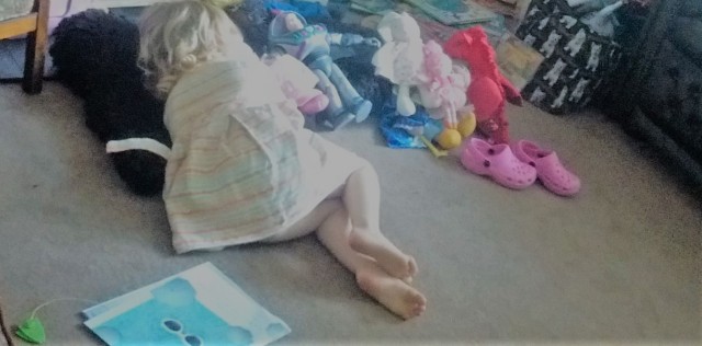 Child lying on a rug snuggled up to a row of toys